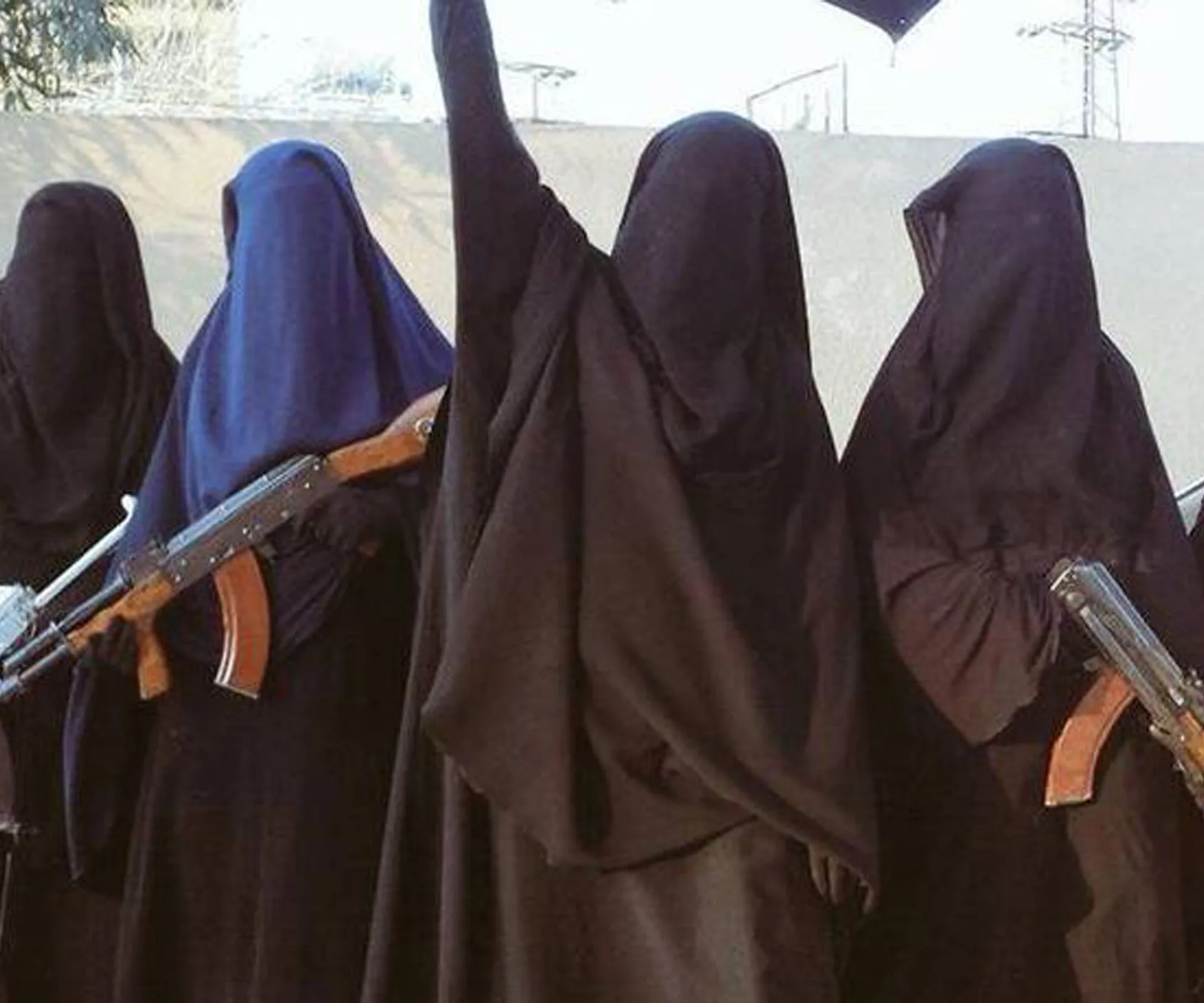 Women in black robes and headscarves, some with rifles, standing in a group with one raising an arm.