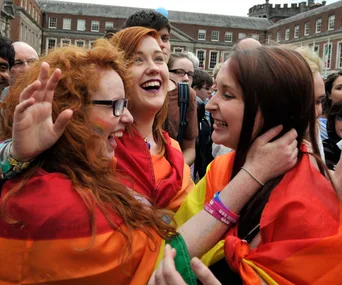Women celebrating with rainbow flags at a same-sex marriage equality event.