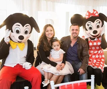 Family sitting with Mickey and Minnie Mouse mascots at a birthday party.