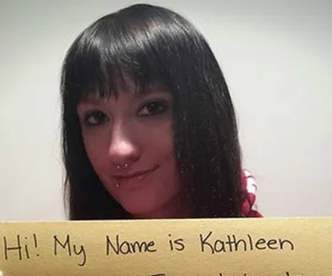 Young woman holding a sign that reads "Hi! My Name is Kathleen," searching for her birth mother.