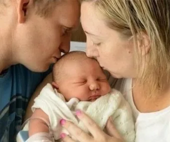 A couple kisses their newborn wrapped in a blanket.