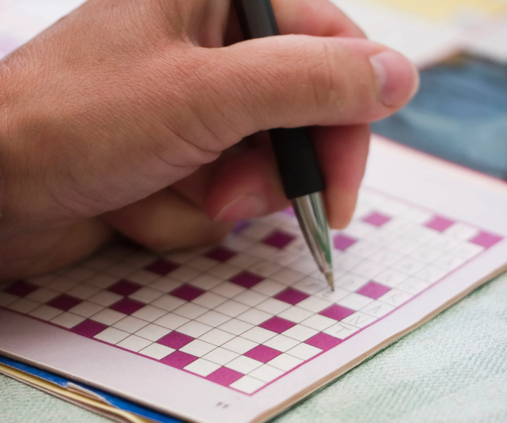 A person solving a crossword puzzle in a book with a pen.