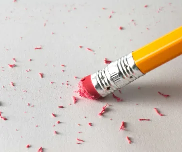 Pencil eraser with pink shavings on paper, symbolizing corrections and mistakes in writing.