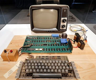 Apple I computer with TV display, motherboard, and keyboard on a wooden table setup for demonstration.