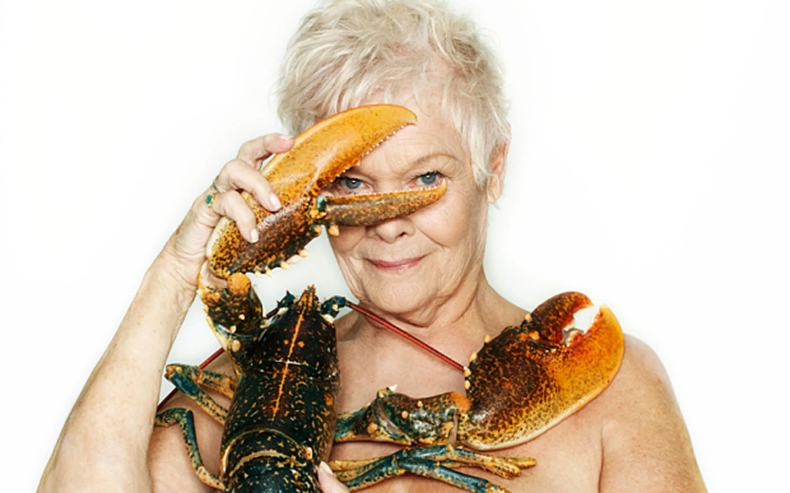 Elderly woman humorously posing with a large lobster, using one claw to playfully cover one eye.