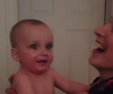 Baby looks surprised while being held by an adult, both smiling and joyful.