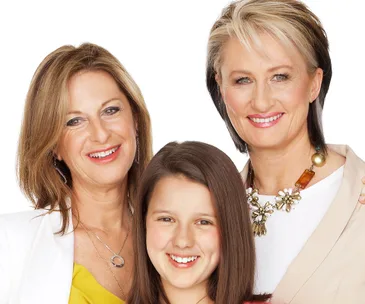 A happy young girl smiling with two women, all appearing joyful and engaged.