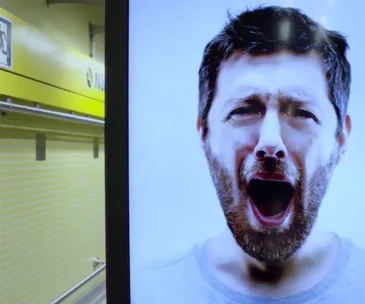 A yawning man's face on a billboard in a subway station with yellow tiles.