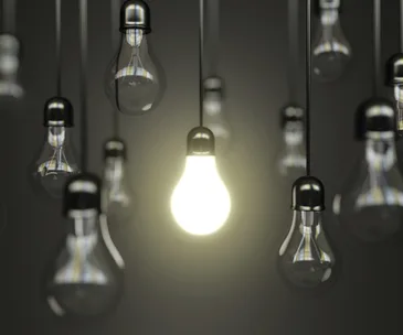 Alt text: "Brightly lit bulb among several dim ones, symbolizing discovery or innovation."