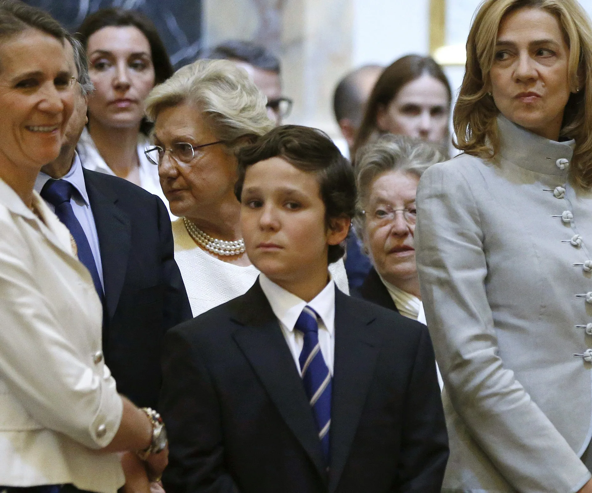 A group of people, including a young boy in a suit, stand in a formal setting.