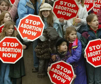 Children holding "Stop Abortion Now" signs at a protest.