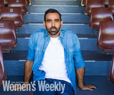 Man in a denim shirt seated on stadium steps, looking at the camera, featured in The Australian Women's Weekly.
