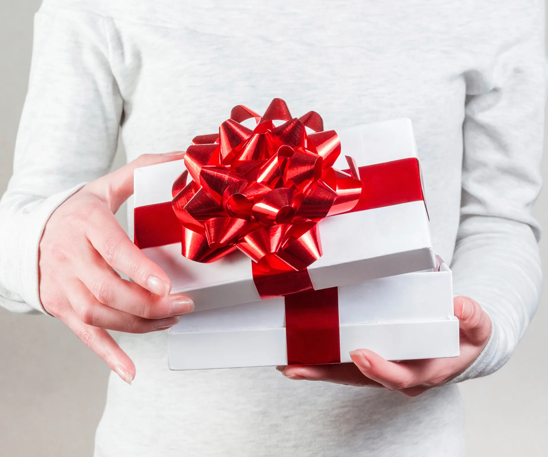 A person holding a white gift box with a red ribbon.