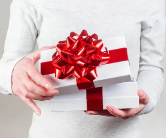 A person holding a white gift box with a red ribbon.