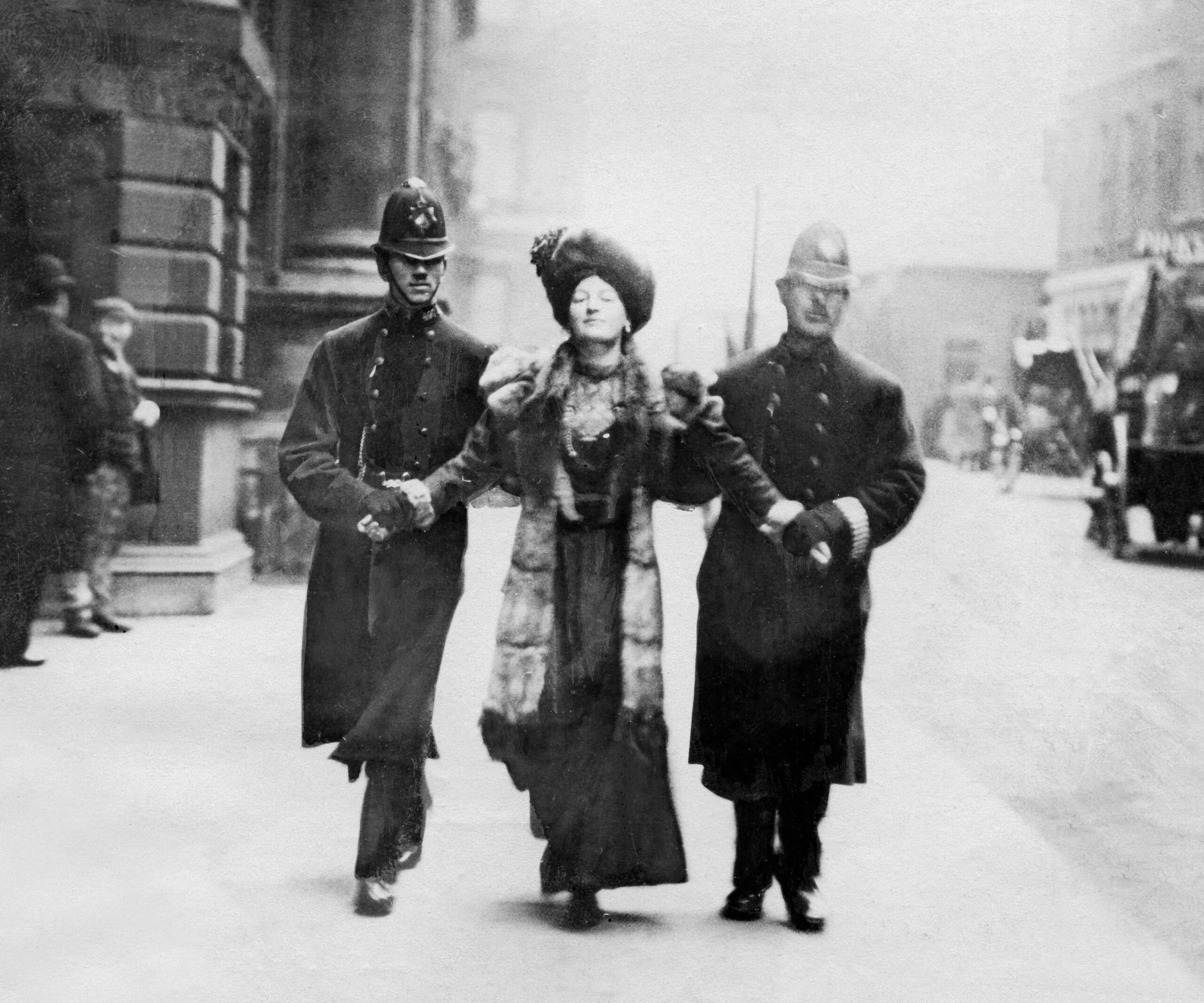A suffragette being escorted by two policemen on a city street, early 1900s.