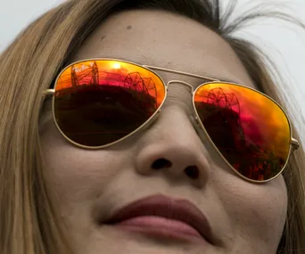 Woman wearing reflective sunglasses with stadium reflected in lenses.
