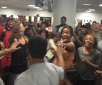 Crowd smiling and singing joyfully during an impromptu 'Lion King' performance at an airport terminal.