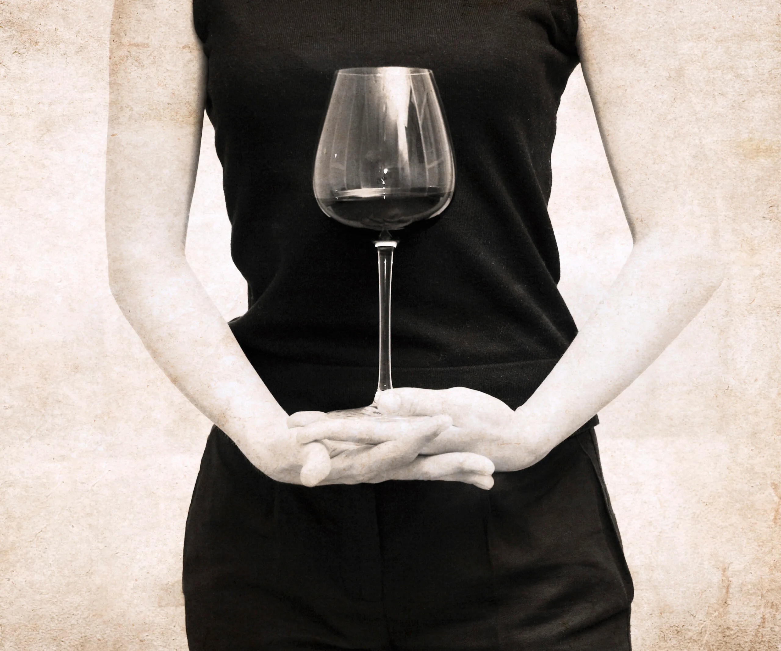 A woman holding a wine glass in front of her body, wearing a sleeveless black top, arms crossed.