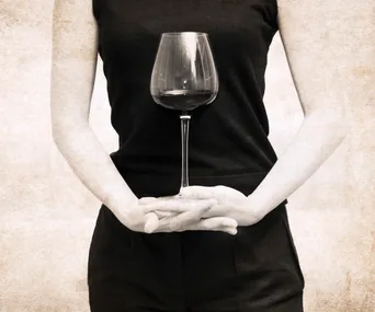 A woman holding a wine glass in front of her body, wearing a sleeveless black top, arms crossed.