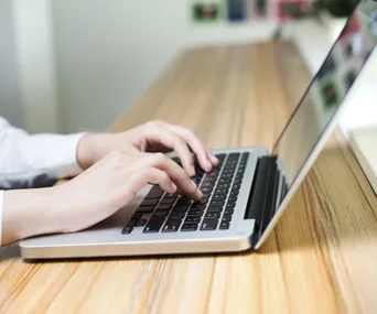 Person typing on a laptop at a wooden desk, focused workspace atmosphere.