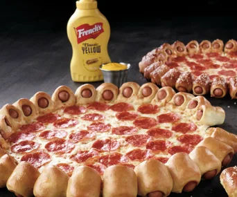 Pepperoni pizza with hot dog crust, mustard bottle, and dip on a black background.