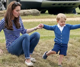 Kate and young Prince George play in the grass at a polo event, holding hands.