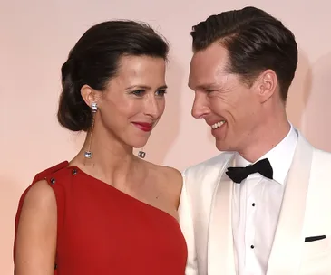 Couple smiling together; woman in red dress with long earrings, man in white tuxedo with bow tie.