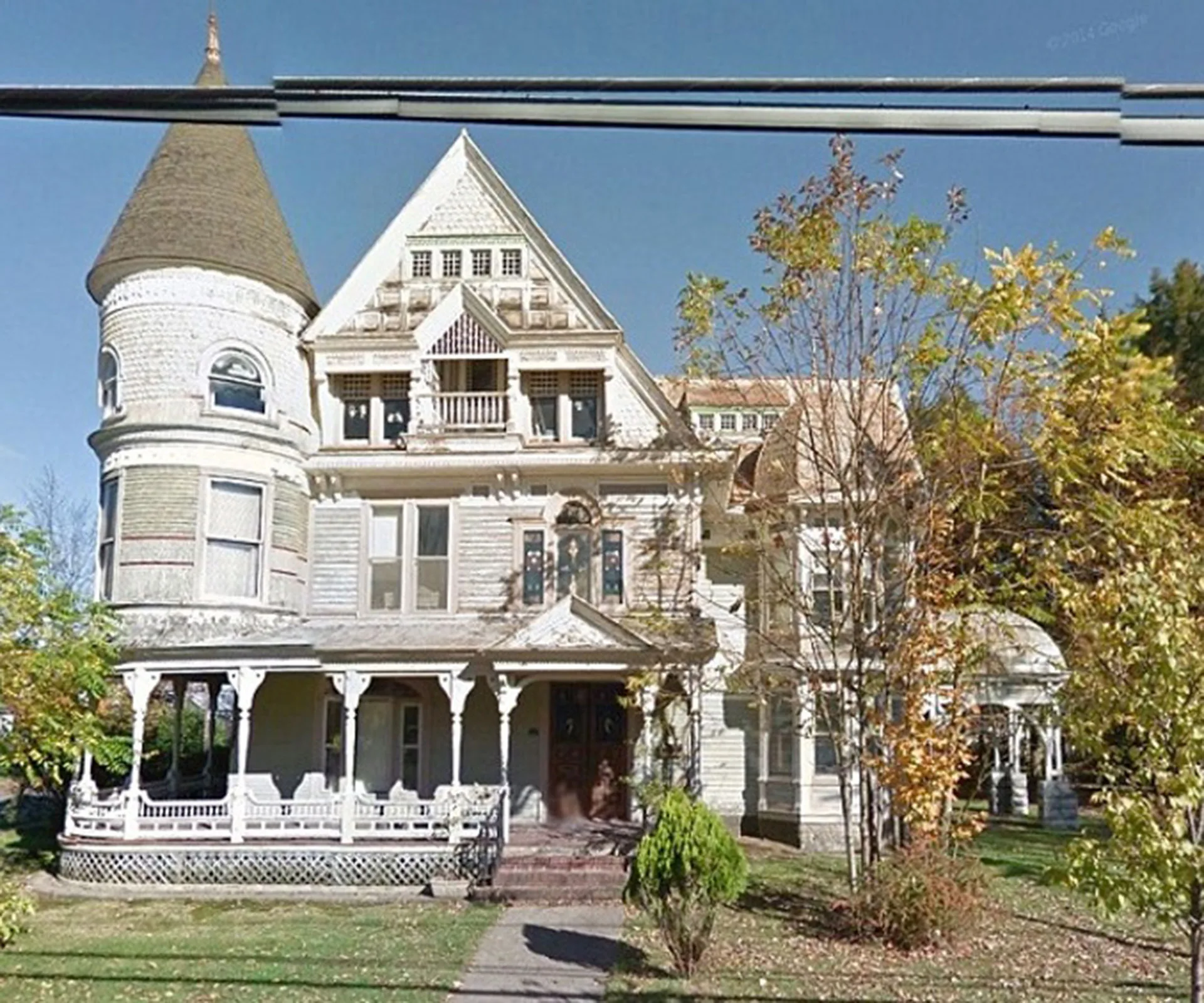 Victorian-style haunted house with a tower and porch, surrounded by autumn trees.