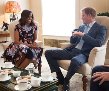 Two people sitting in armchairs engaging in a conversation, with tea and biscuits on the table in front of them.