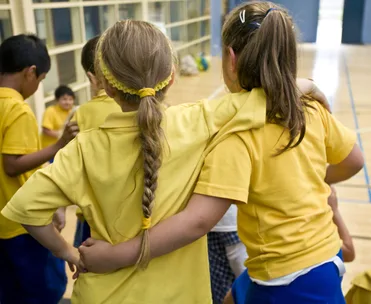 Children in yellow shirts with arms around each other, standing indoors, showing friendship and camaraderie.