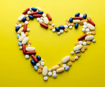 Heart shape made of various pills on a yellow background.