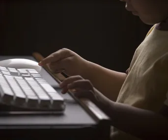 Child using a computer keyboard in a dimly lit room.