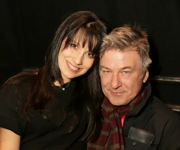 A smiling couple, one with long dark hair and the other with short light hair, posing closely together.