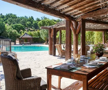 Covered outdoor dining area near a pool in a lush garden setting.