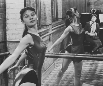 Ballerina practicing at a barre with a teacher observing in a dance studio.