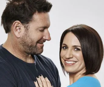 A smiling couple standing close, the man looking at the woman who faces the camera, both appearing cheerful.