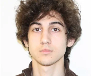 Person with curly hair and a neutral expression, wearing a zip-up jacket, against a plain background.