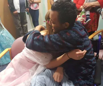 A young couple embraces, surrounded by supportive friends and family in a warmly lit room, symbolizing love and support.