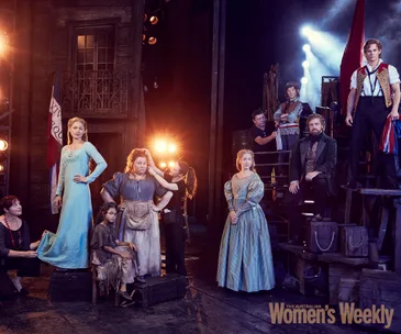 Cast of Les Misérables in costume backstage, with period attire and stage props, preparing for a theatrical performance.