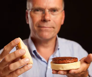Person holding a test-tube burger in a bun, ready to assemble.