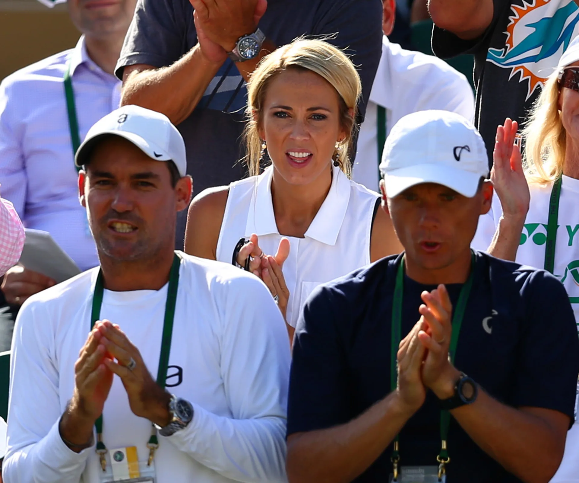Spectators, including a woman in white, clap at a tennis match, expressing support and anticipation.