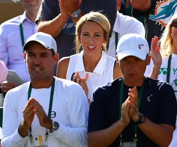 Spectators, including a woman in white, clap at a tennis match, expressing support and anticipation.