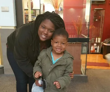 A woman and child smiling in a brightly lit room, standing in front of a glass display.
