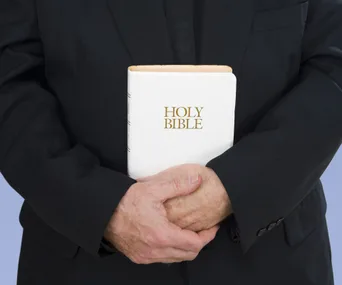 Man in black suit holding a white Holy Bible in his hands.