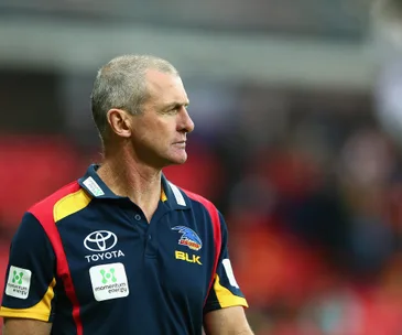 AFL coach in Adelaide Crows polo shirt on field, looking to the side.