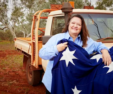 Australian woman in blue shirt holding flag near utility truck in rural setting.