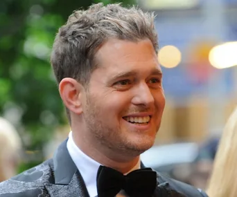 Smiling man in a suit and bow tie, outdoors with a blurred background.
