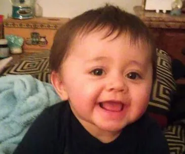 A smiling baby lying on a patterned blanket, with a blue towel beside them.