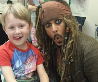 Young boy smiles with excitement as a pirate character poses animatedly beside him.