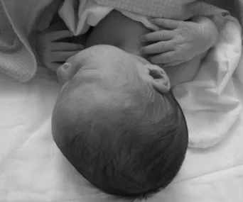 Newborn baby sleeping, wrapped in a blanket, with tiny hands near the chest; black and white photo.